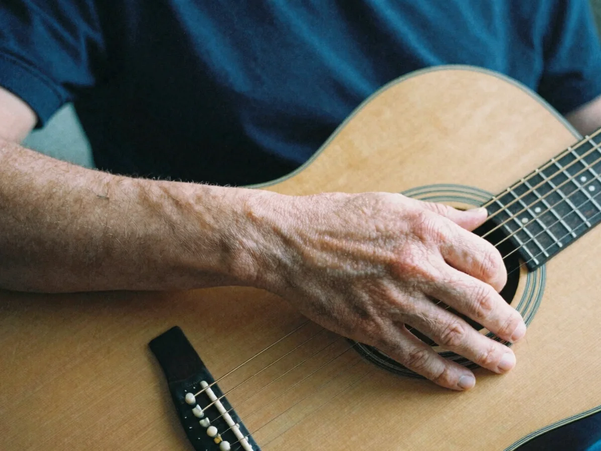 Close-up editorial photograph of hands resting on an acoustic gui